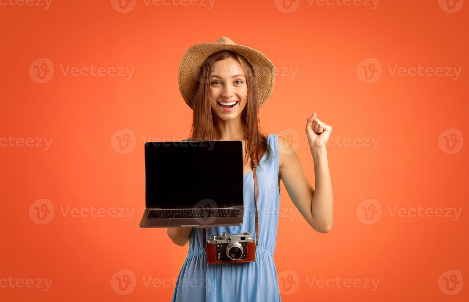 Cheerful girl traveller holding laptop with empty screen over yellow background, website for travellers and tourists photo
