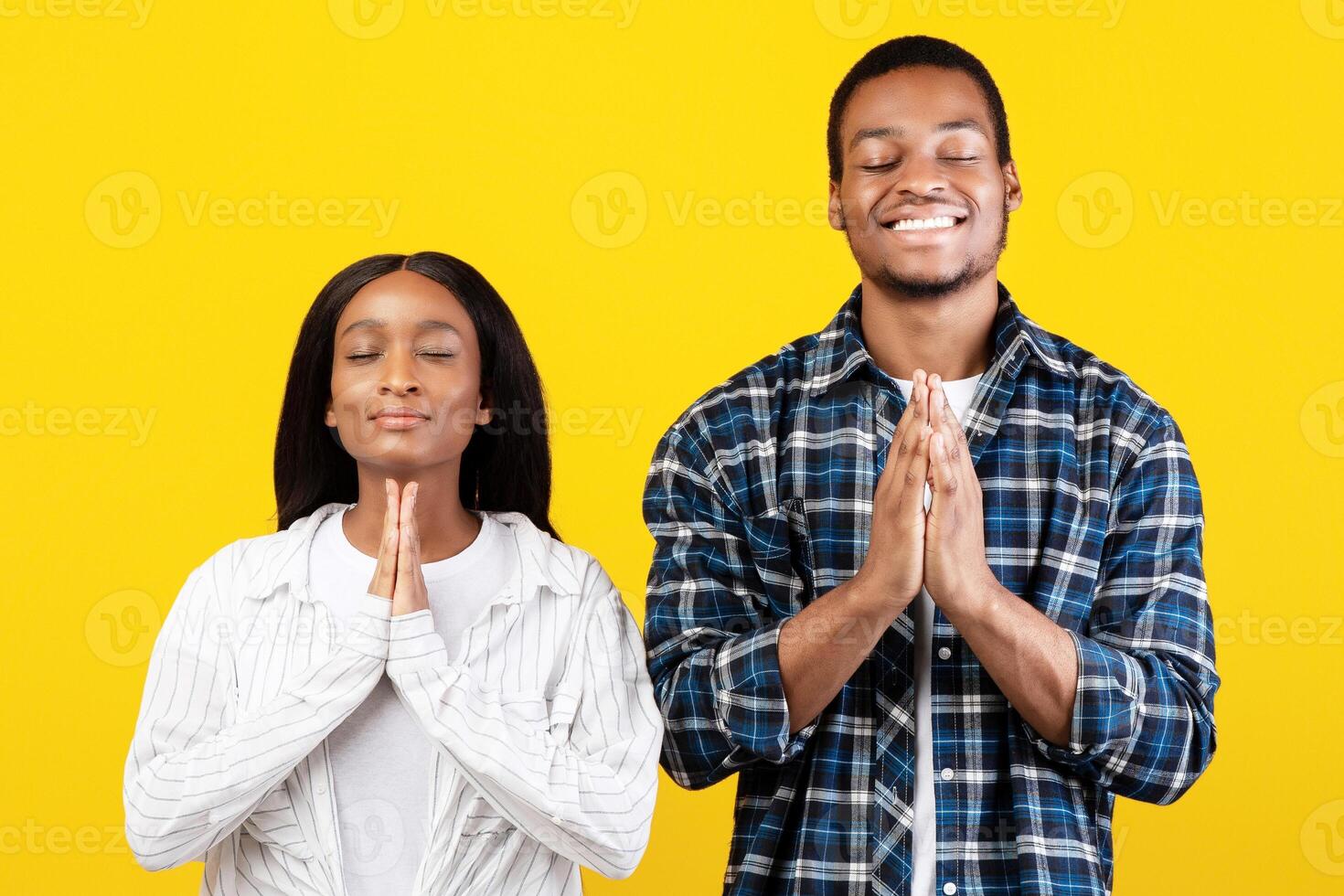 Pray, ask for fulfillment of desire and very want something. Smiling young african american family folded their hands and believe in dream, isolated on yellow background, studio shot, free space photo