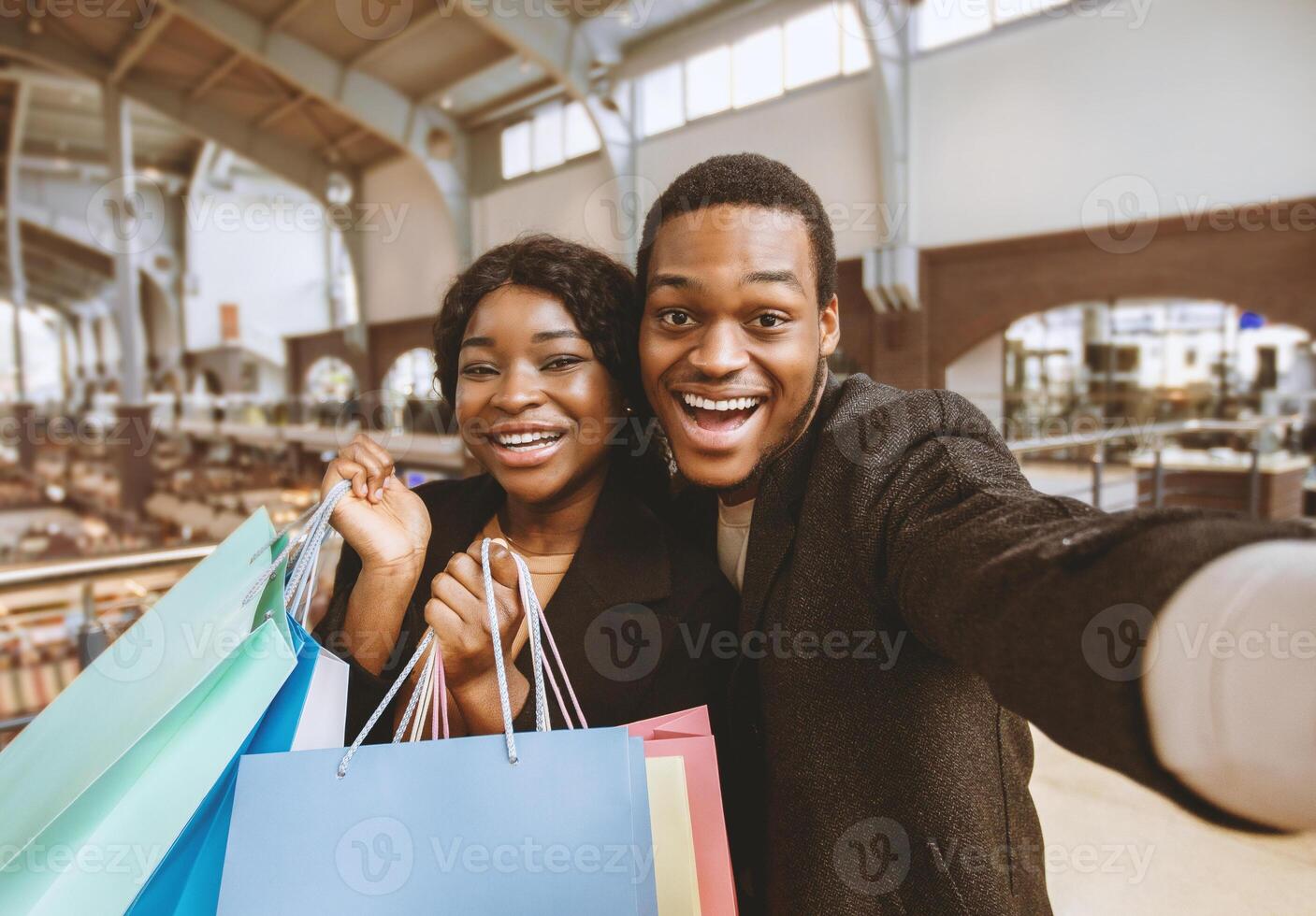 Amorous dates with shopping bags in modern city mall. Portrait of young smiling african american male and female talking during sale on weekend and make selfie at Black Friday and have fun, copy space photo