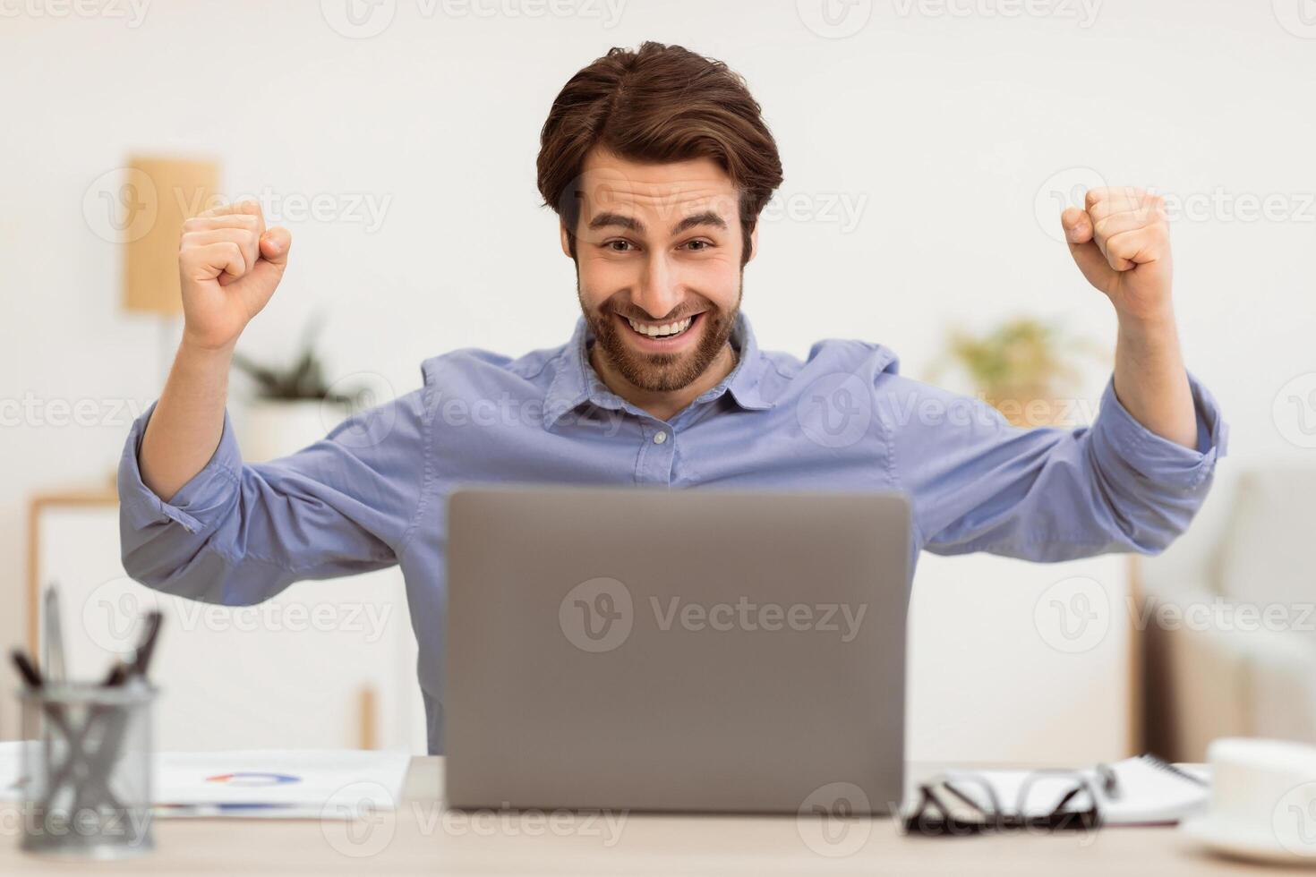 Joyful Man At Laptop Shaking Fists Looking At Computer Screen Celebrating Business Success Sitting At Workplace In Modern Office. Great News And Victory Celebration, Successful Career Concept photo