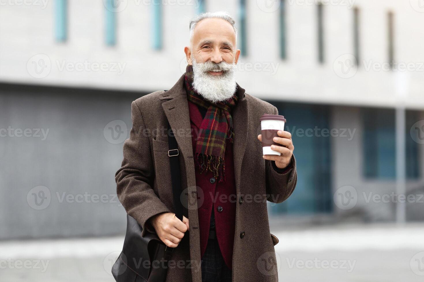 Happy elderly man walking by street, drinking coffee to go in paper cup, smiling at camera, copy space. Cheerful grandfather making sightseeing on weekend, drinking hot tea, warming up photo
