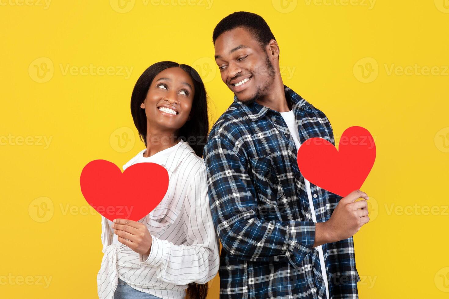 Fun romantic holiday and valentines day celebration. Smiling millennial african american students couple standing back to back, hold big red hearts, isolated on yellow background, empty space photo