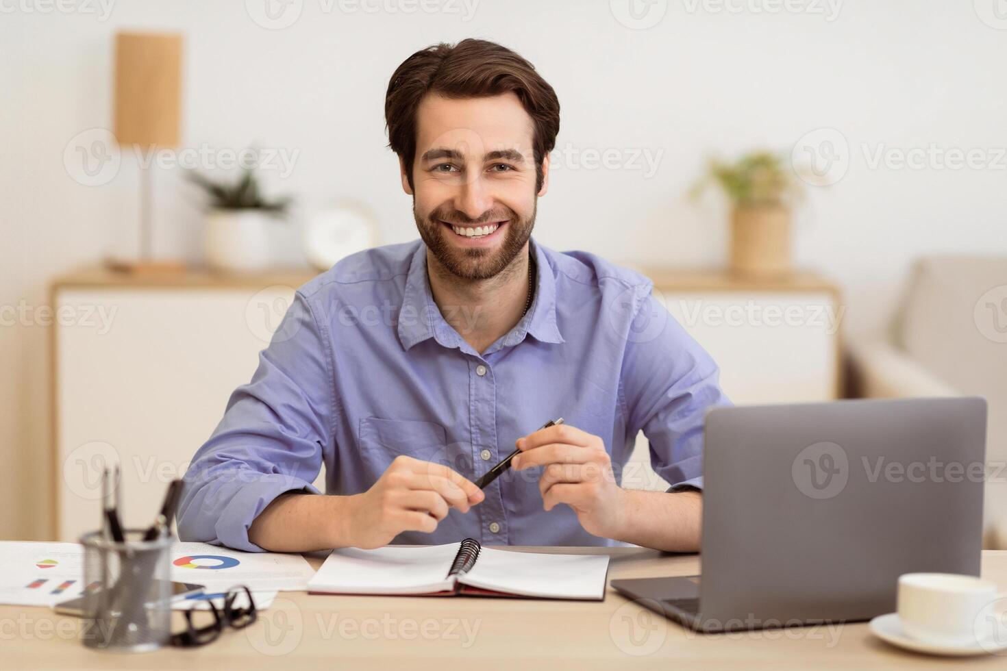 Happy Businessman Posing At Workplace Sitting At Laptop And Smiling To Camera In Modern Office. Entrepreneur's Portrait. Entrepreneurship And Successful Business Career Concept. Selective Focus photo