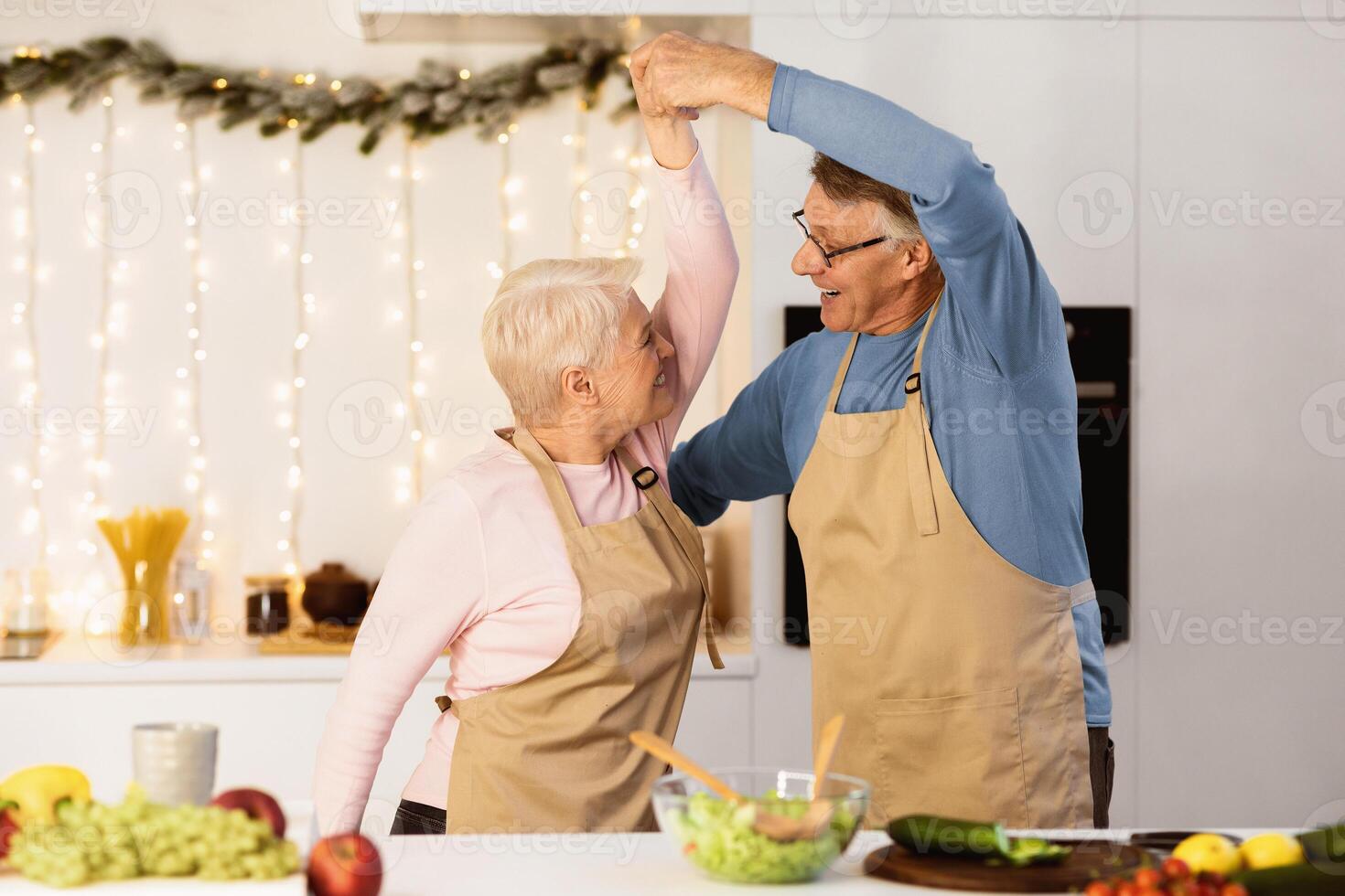 Mature Married Couple Dancing In Kitchen, Having Fun Cooking Together On Christmas Eve. Senior Spouses Enjoying New Year Dinner Preparation At Home. Family Cooks Meal On Winter Holidays Indoors photo