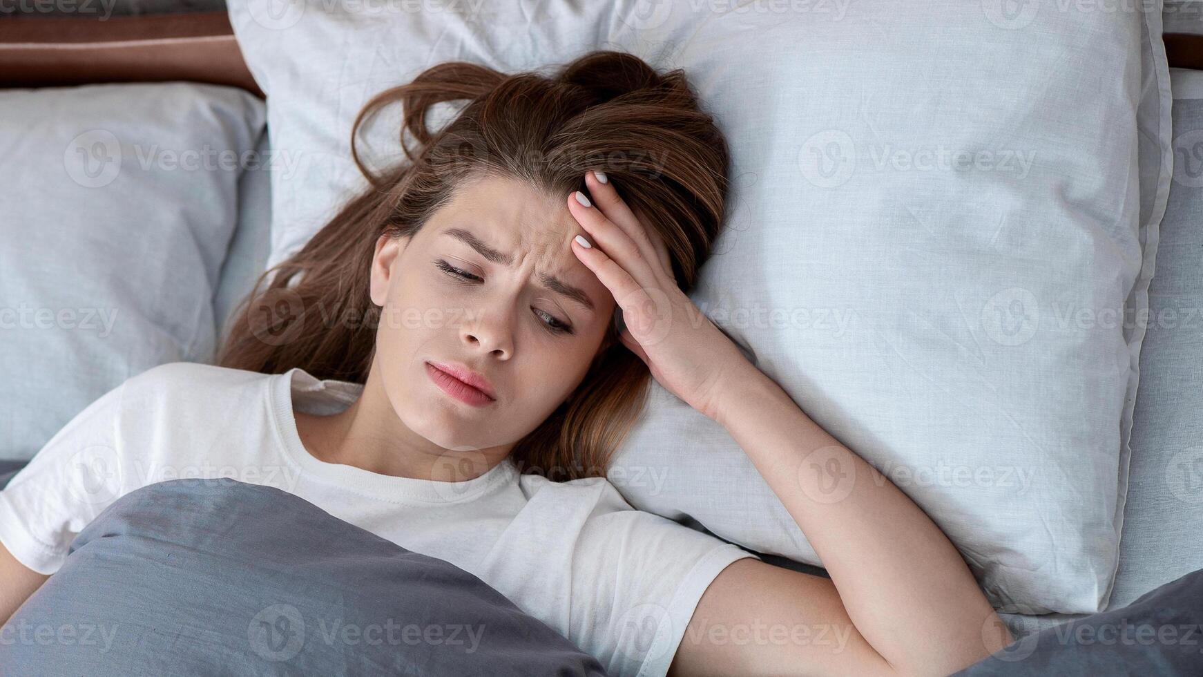 Mental health disorders. Top view of unhappy Caucasian woman lying in bed, suffering from depression, anxiety or insomnia. Stressed lady feeling miserable, lonely or apathic photo