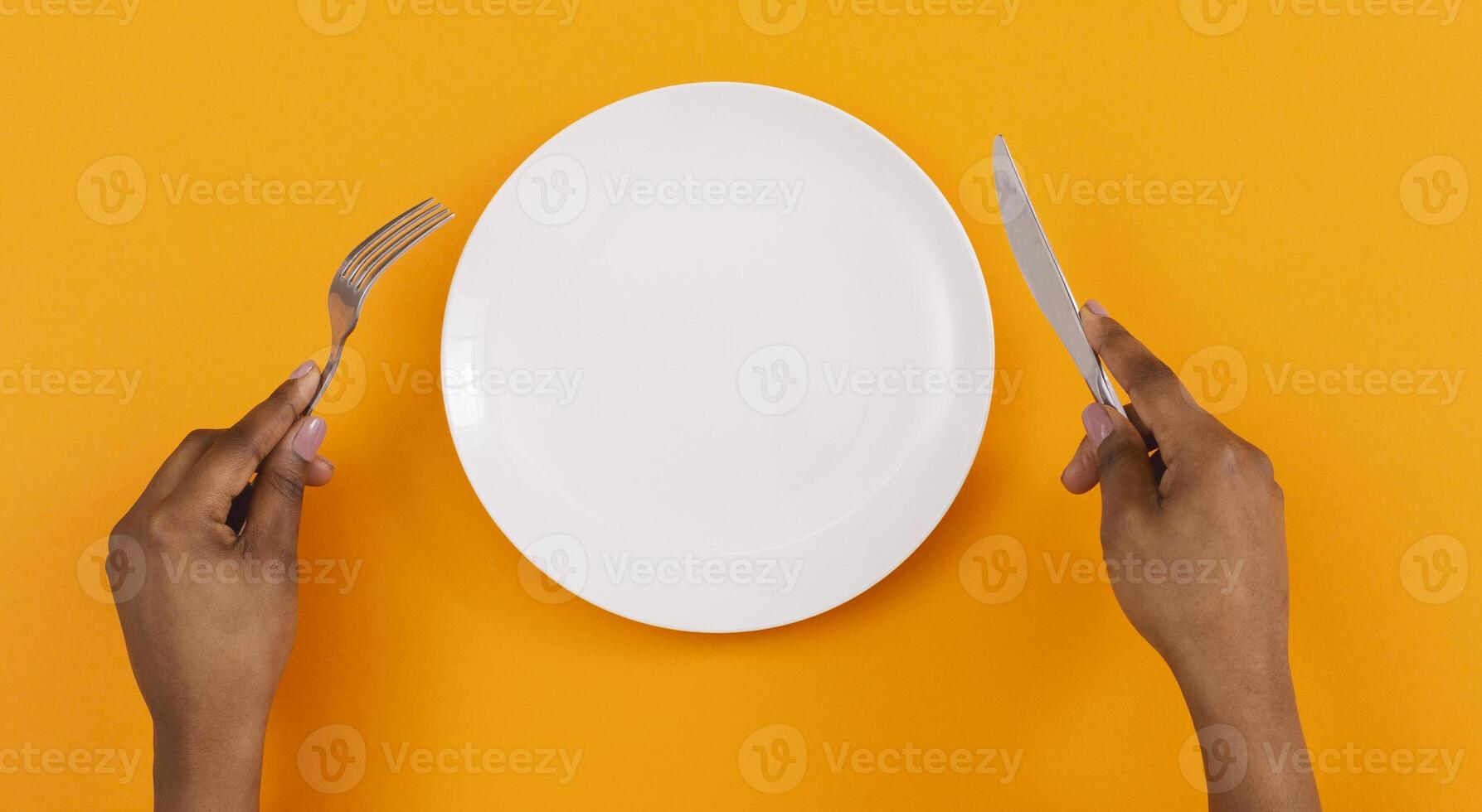 Lunch time. Top view of empty plate with fork and knife in black woman's hands on orange background, panorama photo