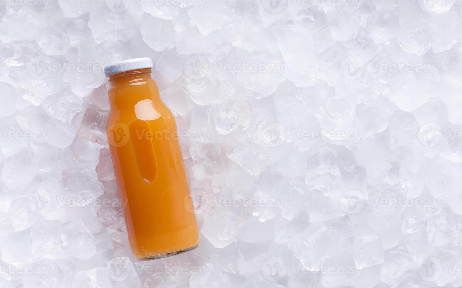 Orange detox juice in glass bottle on ice cubes background, panorama photo