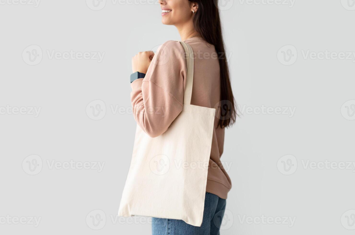 Close Up Of Young Female Consumer Holding Blank White Eco Tote Bag, Posing Standing Over Studio Background. Lady Carrying Flax Tote Shopper Handbag. Eco-Friendly Lifestyle, Stop Using Plastic Concept photo