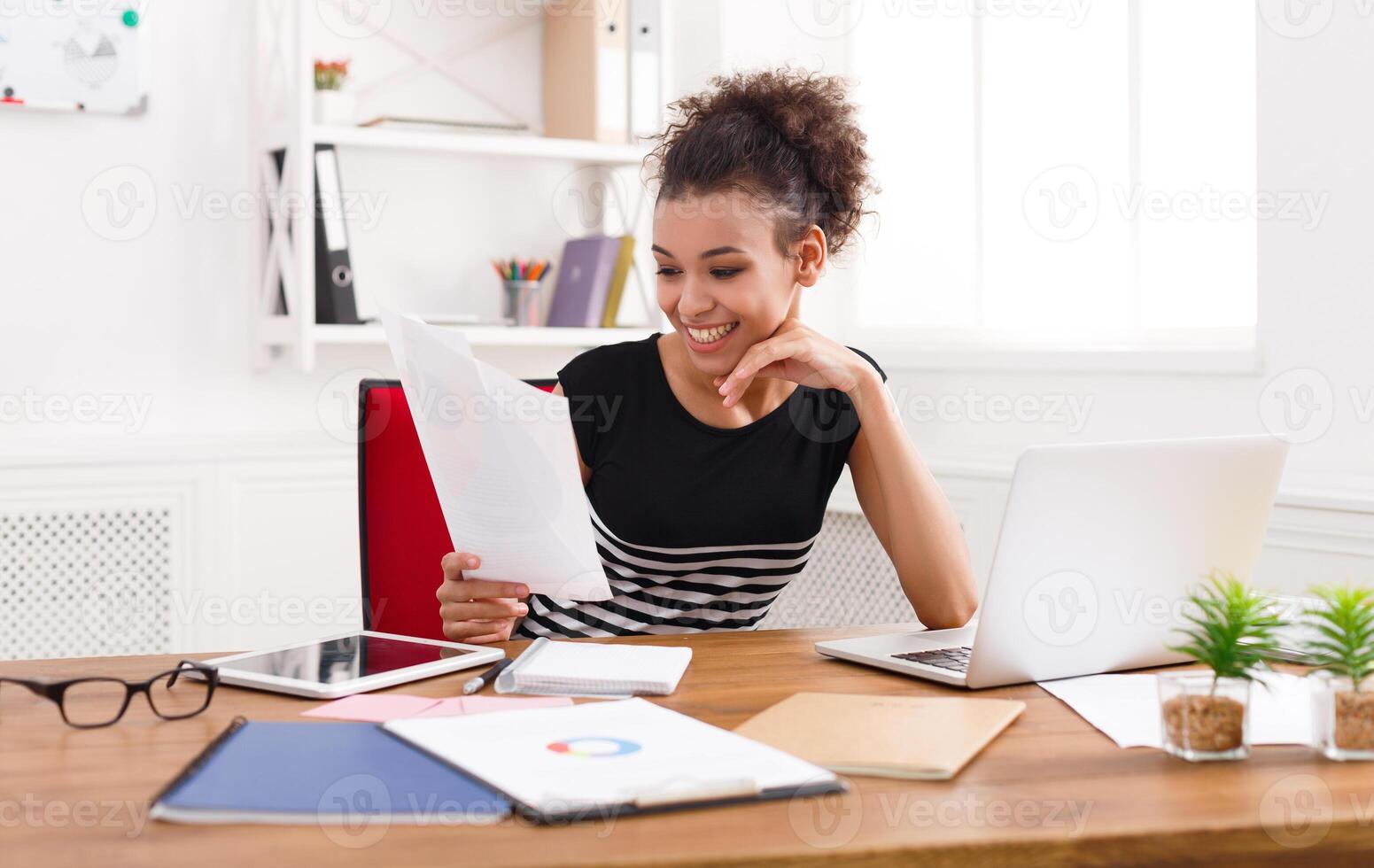 Paperwork. Happy smiling business woman in formal wear sitting at wooden desk in modern office and reading report document. photo