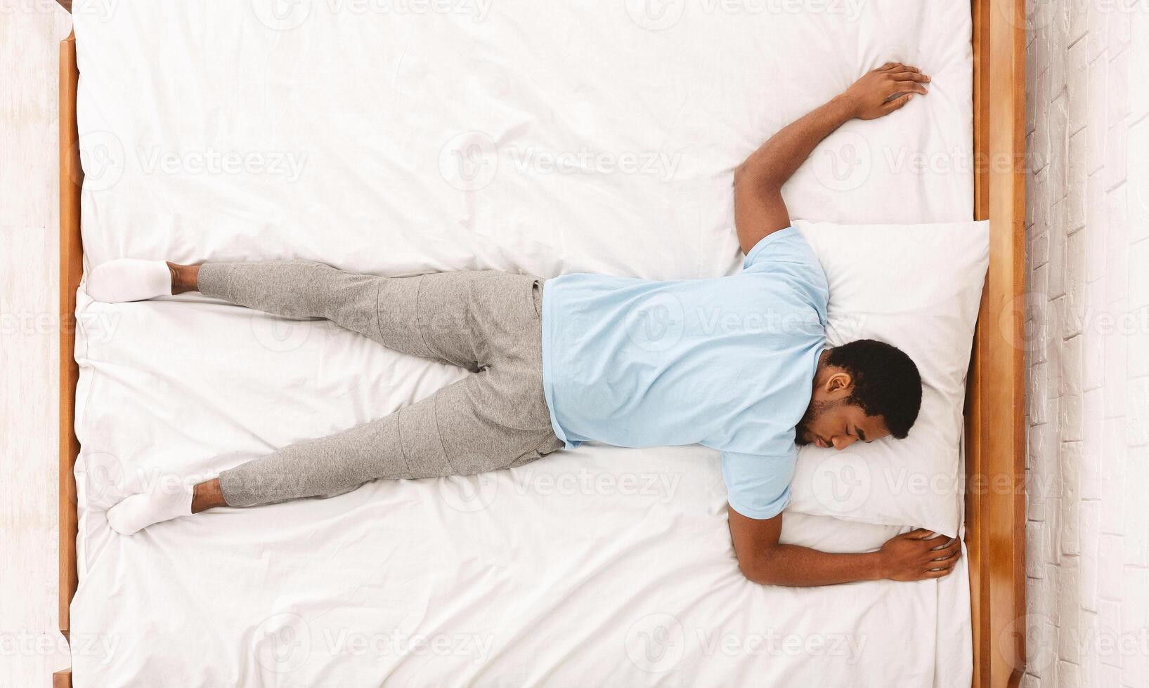 Favorite pose for sleep. African american millennial guy sleeping, lying on stomach in bed, top view photo