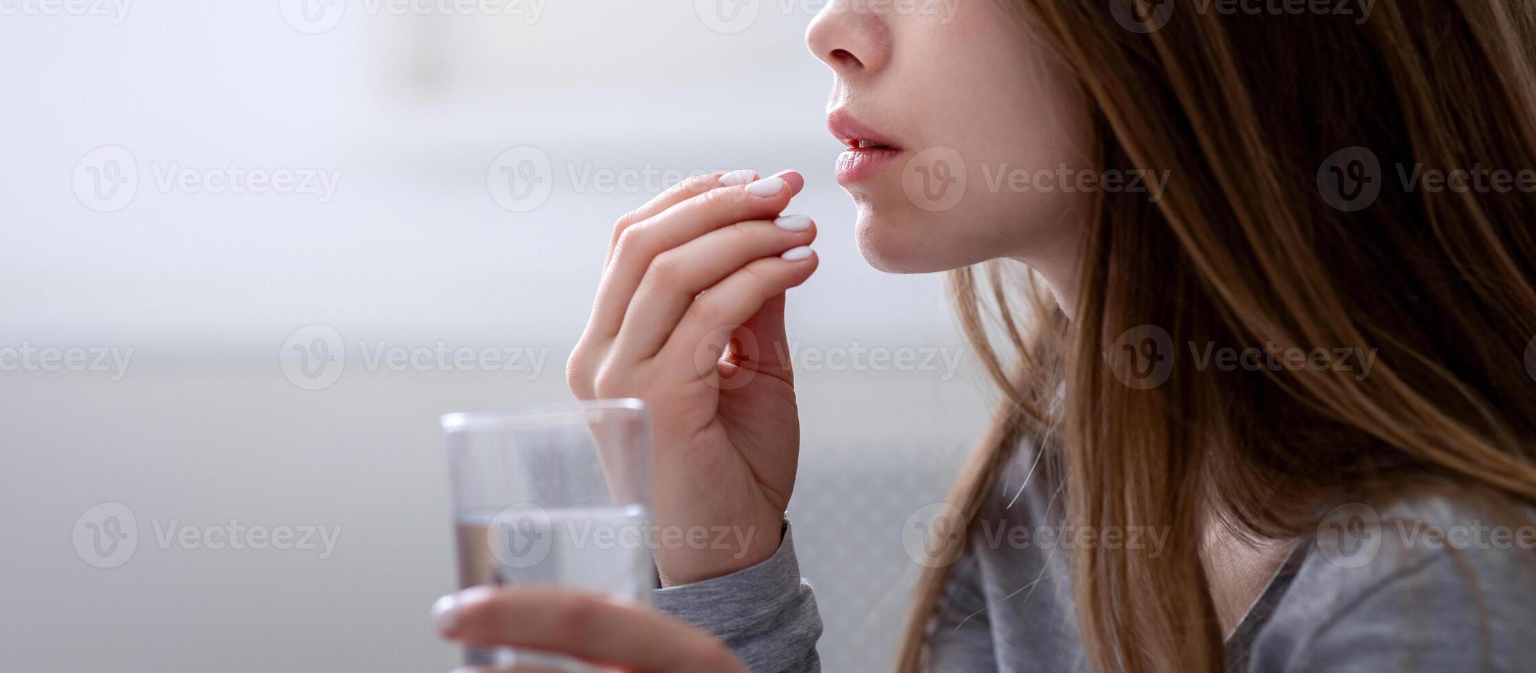 Side view of young woman with glass of water taking sleeping pill or antidepressant, copy space. Millennial lady suffering from insomnia or depression, committing suicide overwhelmed by problems photo