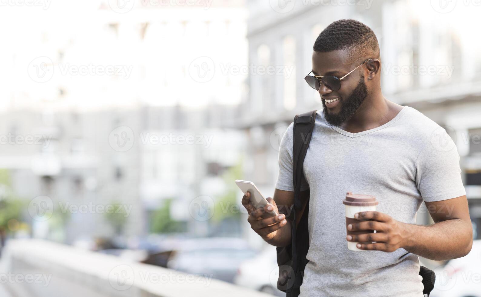 On my way to work. Cheerful bearded african man using his smartphone and drinking coffee, panorama, free space photo
