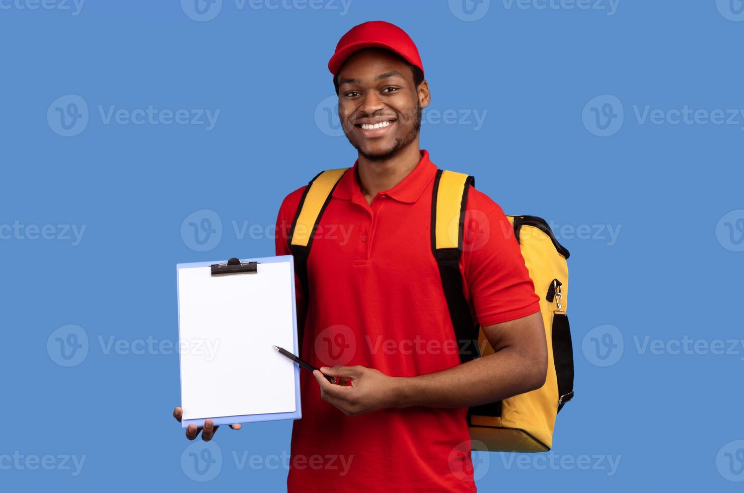 Parcel Receiving. Smiling African American Bearded Delivery Man Holding Pen And Folder With Blank Paper Delivering Goods And Food, Wearing Thermo Bag, Standing Over Blue Studio Background. Mockup photo