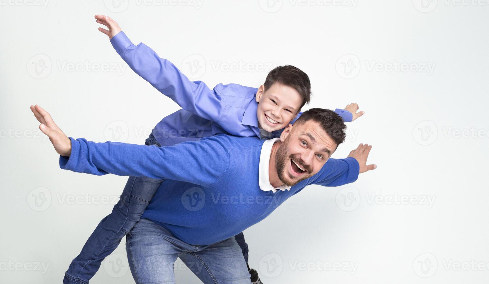 Young father and son playing together, dad riding boy on back, simulating plane, white studio background, panorama photo