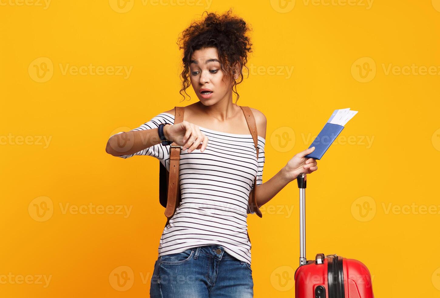 Black Traveler Girl Being Late For Flight Checking Time Standing With Suitcase And Tickets Over Yellow Background. Studio Shot photo