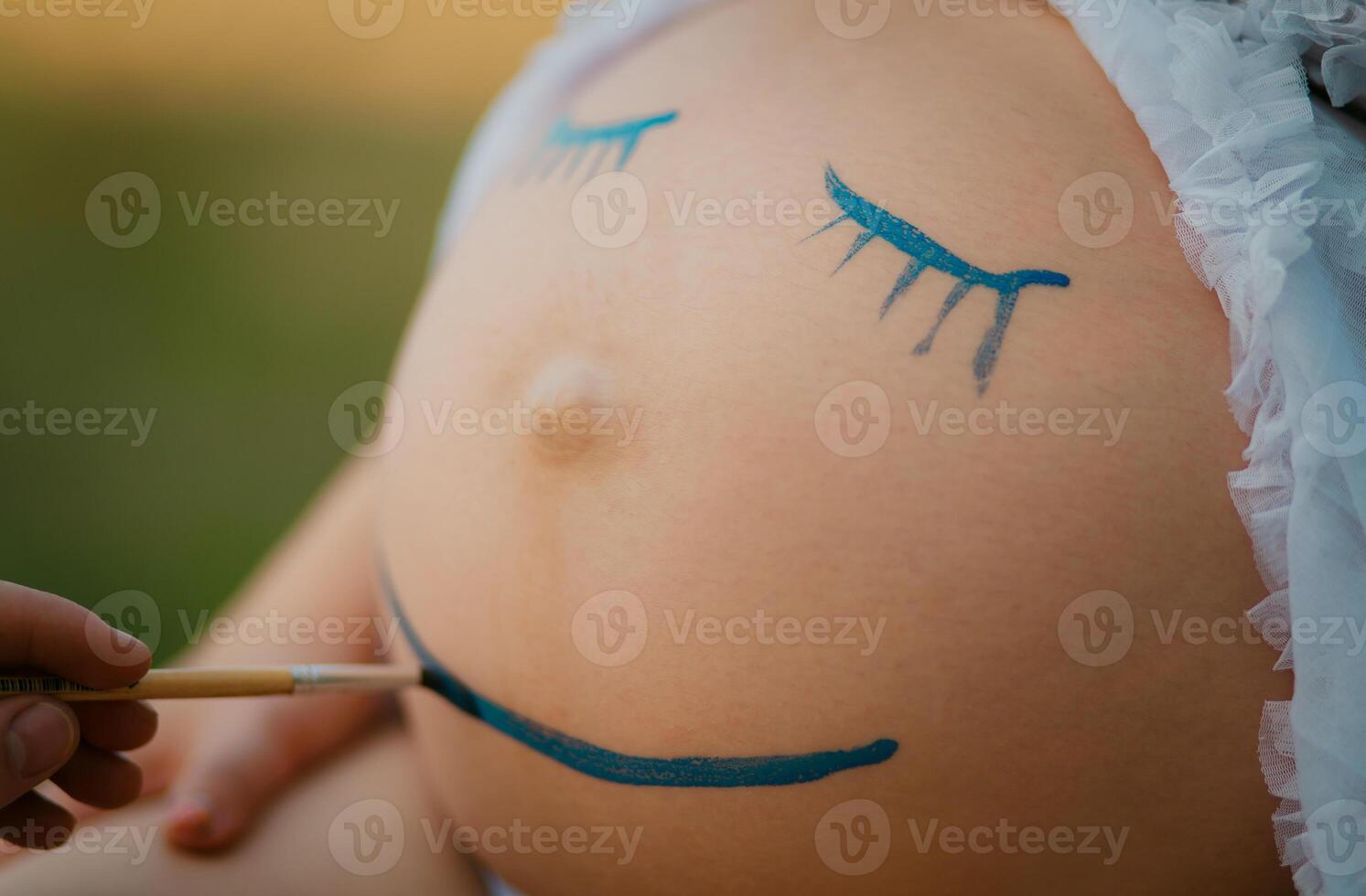 Pregnant woman belly closeup with smiling funny face drawing photo