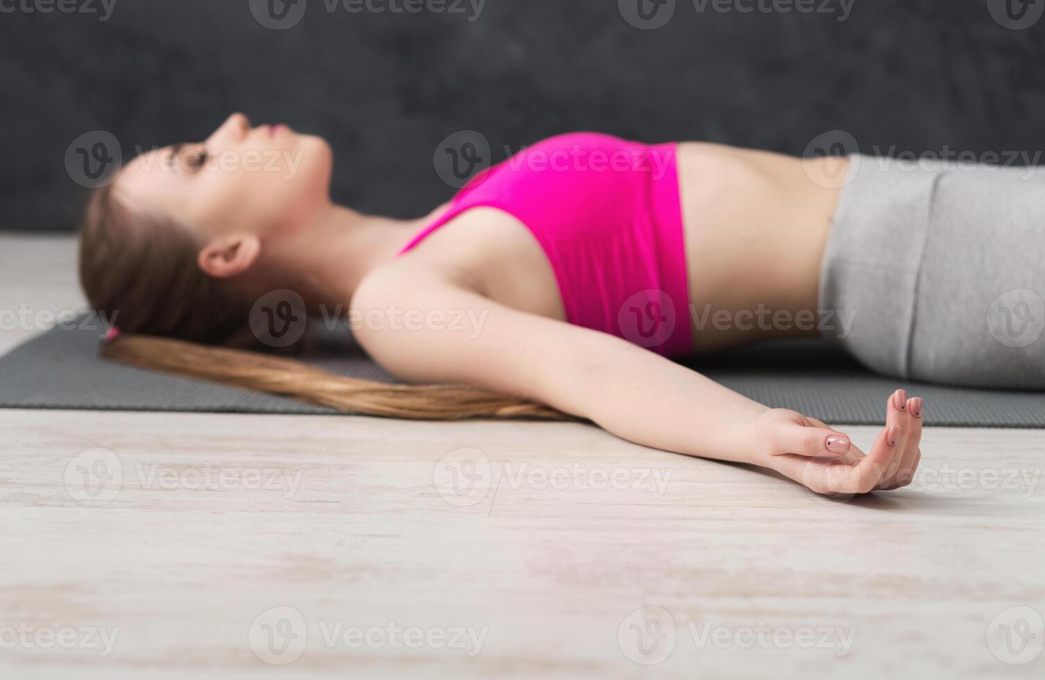 Fitness, woman having rest after training yoga in gym, lying on mat at grey background, copy space, selective focus on hand. Young slim girl makes exercise. photo