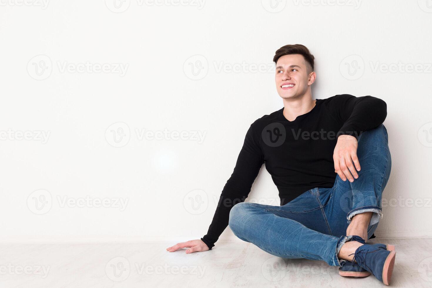 Smiling young man looks up, sitting on the floor at white background, copy space photo