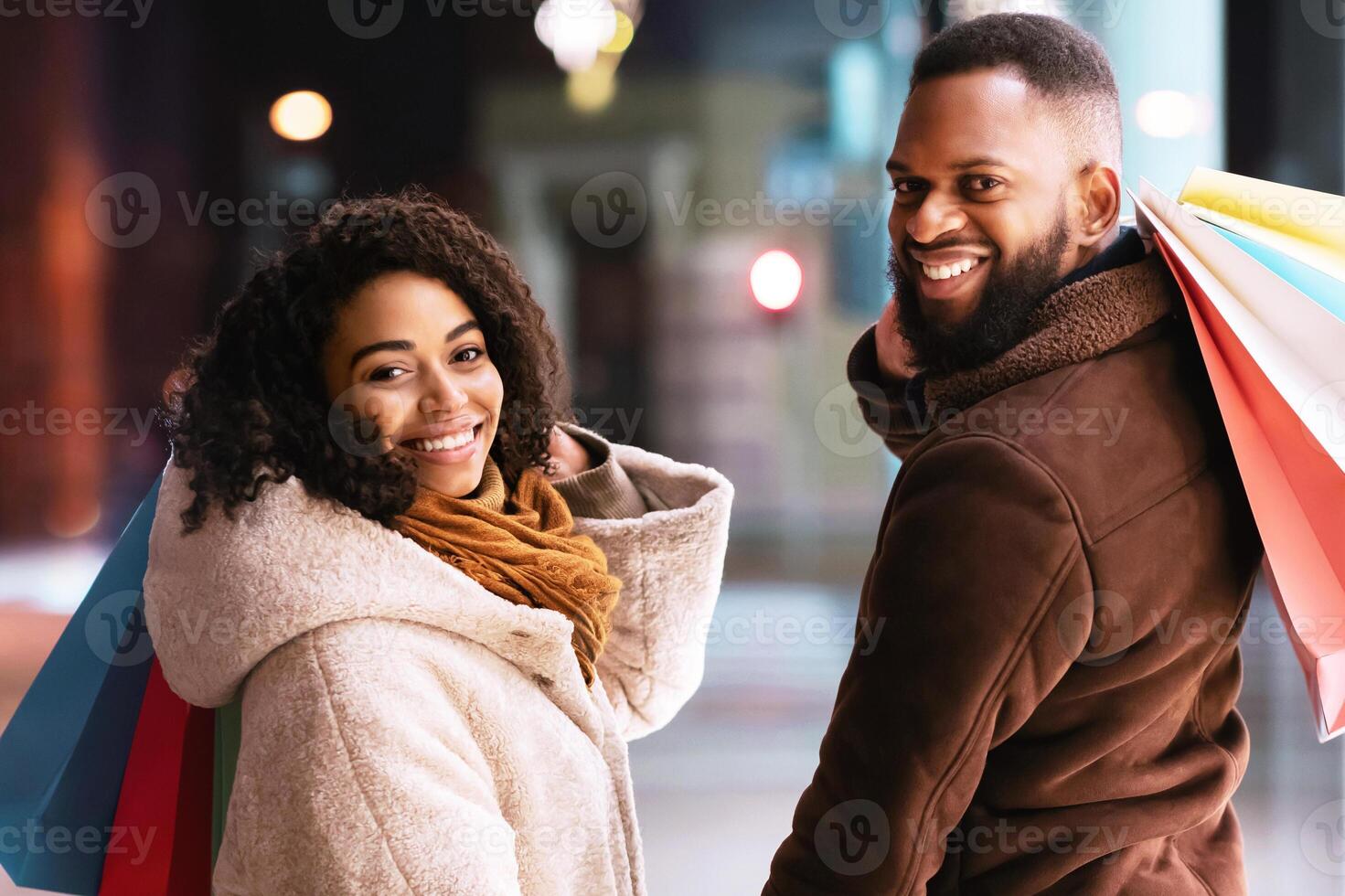 Happy Loving Family. Portrait of smiling black man and woman turning back and looking at camera over the shoulder holding hands, carrying shopping bags. Cheerful african american couple near mall photo
