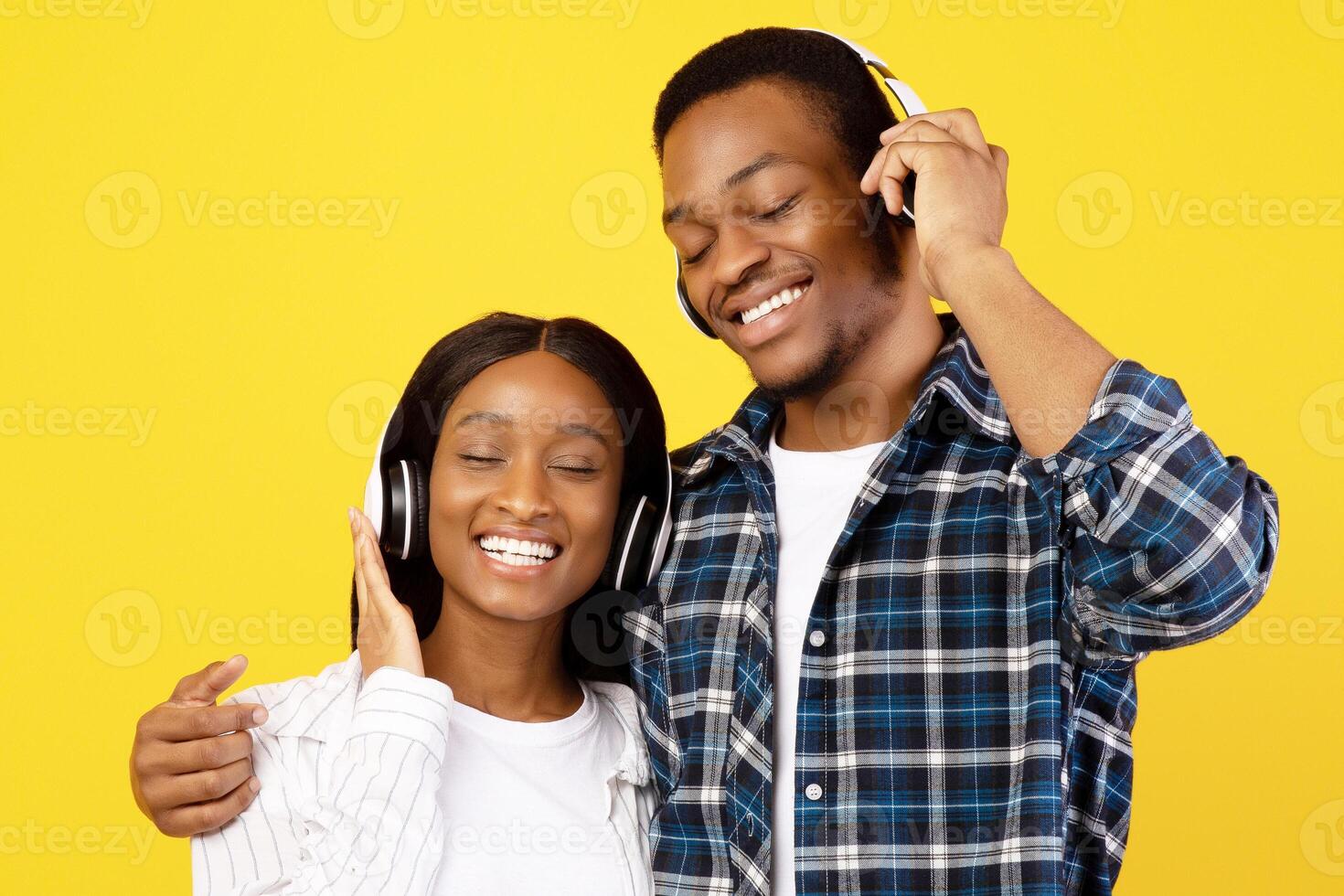 Favorite music together and stay home at covid-19. Smiling young african american couple in love in wireless headphones enjoy song at free time, isolated on yellow background, studio shot, copy space photo