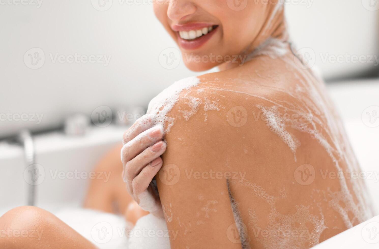 Unrecognizable Lady Washing Body Applying Soap Sud On Skin Touching Shoulder While Taking Bath In Modern Bathroom At Home. Bodycare Cosmetics Concept. Cropped, Selective Focus photo