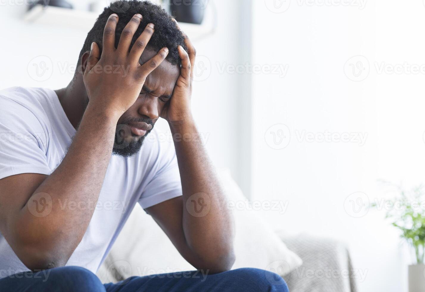 Lonely depressed african american guy sitting at home, suffering from terrible headache, holding head in hands, empty space photo
