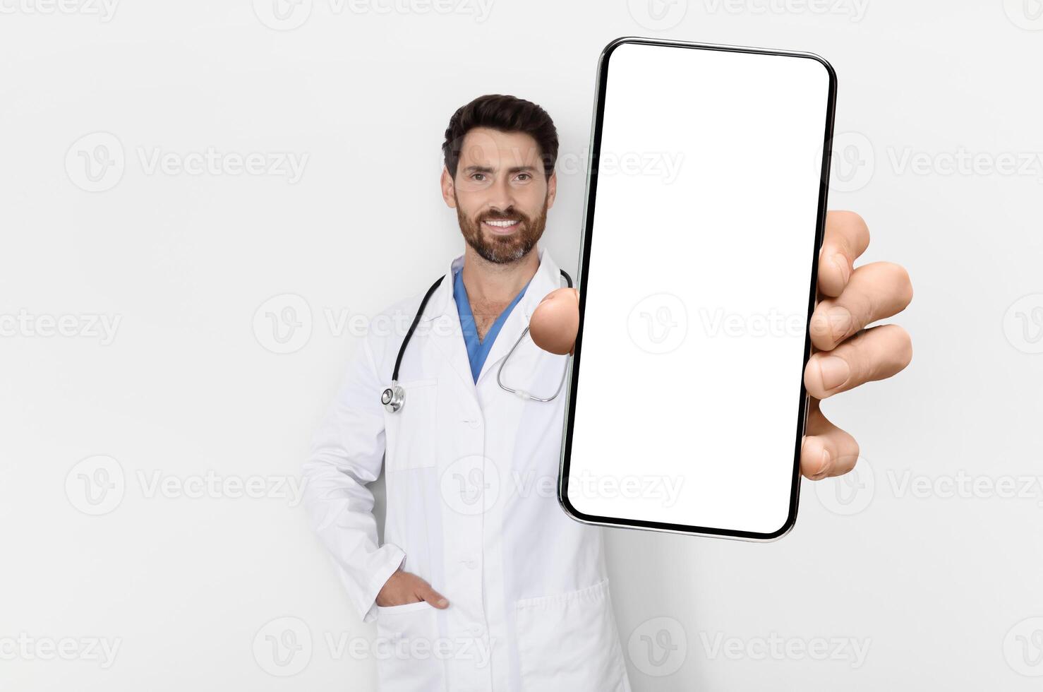 Medical App. Handsome Male Physician In Uniform Demonstrating Big Blank Smartphone At Camera, Smiling Doctor Man With Empty Cellphone In Hand Standing Over White Background, Mockup, Collage photo