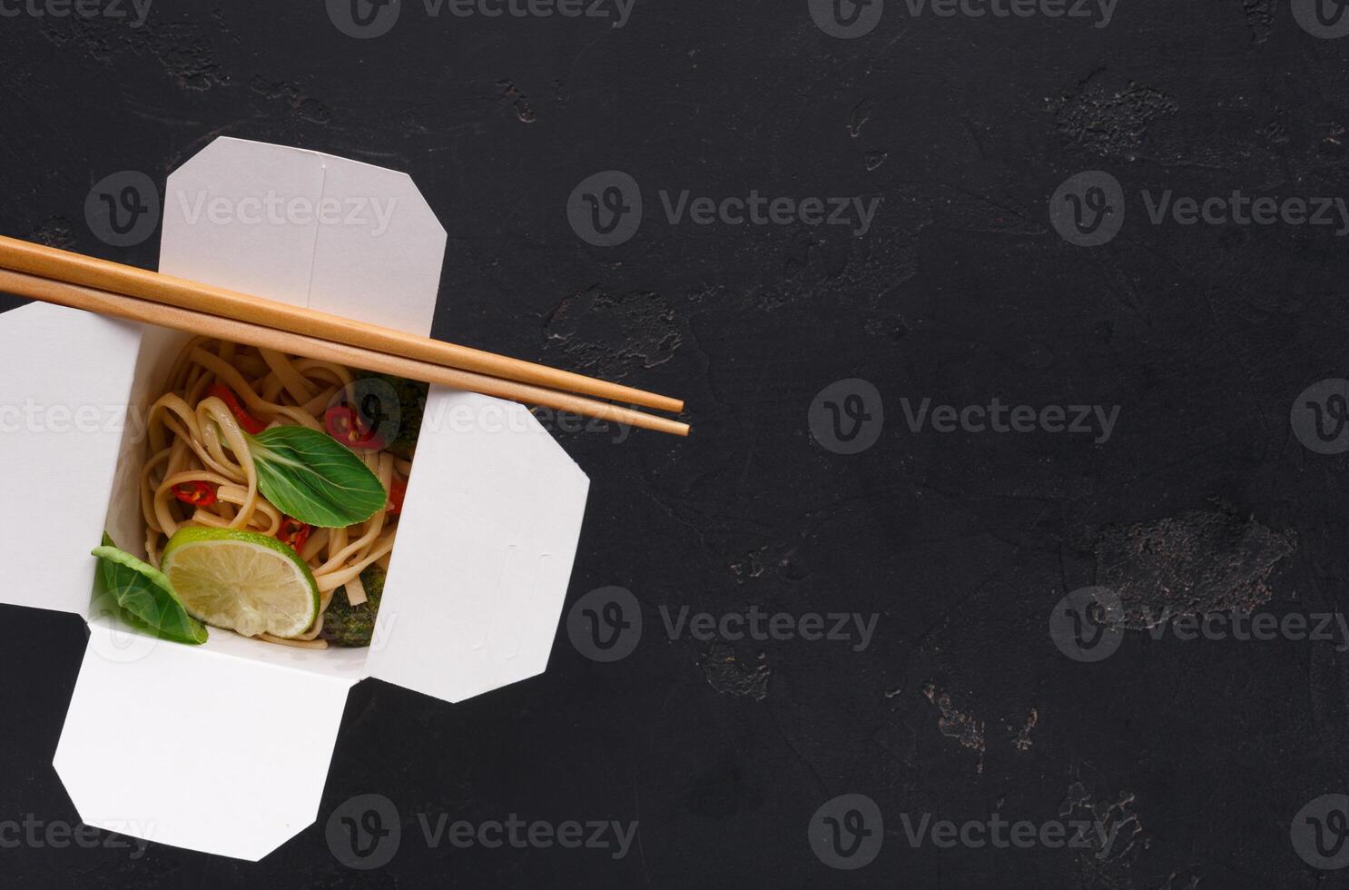 Asian restaurant food delivery. Vegetarian stir fry with noodles, broccoli and green spinach on black background, top view, copy space photo