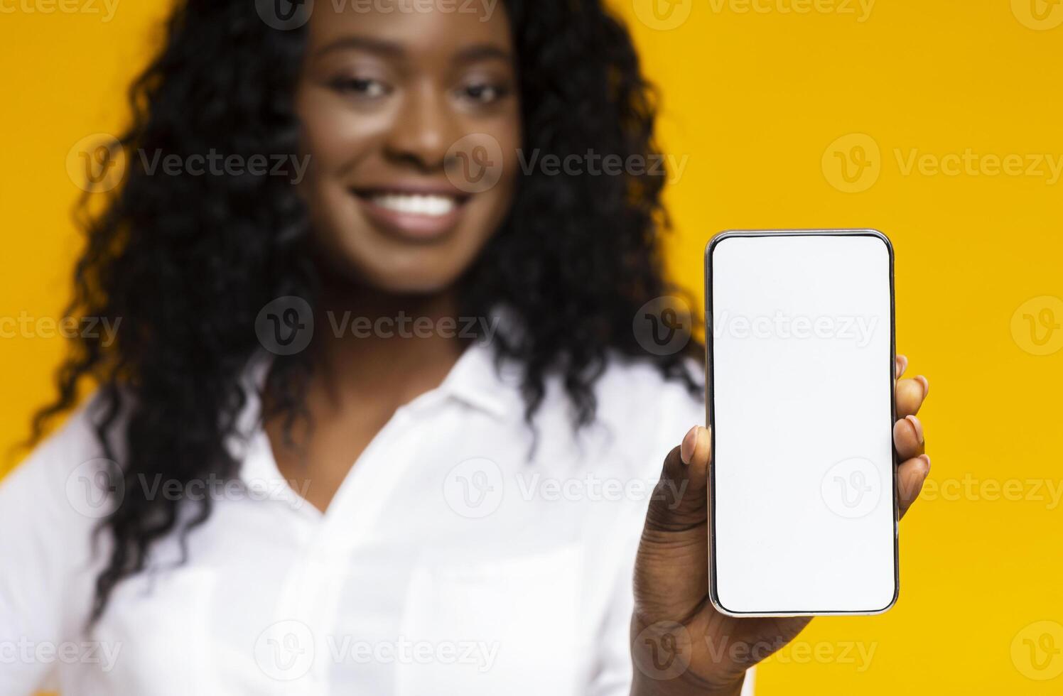 I like this cellphone. Millennial african-american girl showing mobile phone with blank screen, yellow background photo