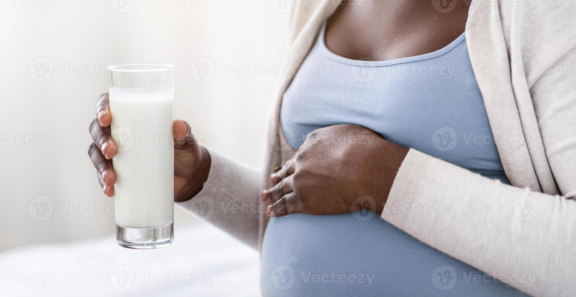 Dairy Products During Pregnancy. Black Pregnant Woman Holding Glass With Milk And Touching Belly, Young Expectant Mother Enjoying Drinking Healthy Calcium Drink While Relaxing At Home, Cropped Image photo