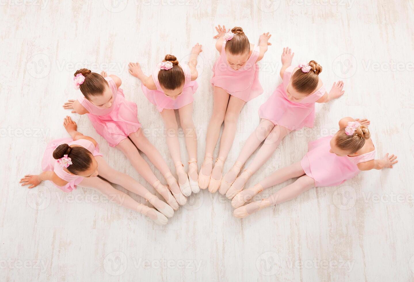 Little ballerinas in ballet studio, top view. Group of girls practicing position sitting on floor, classical dance studio photo