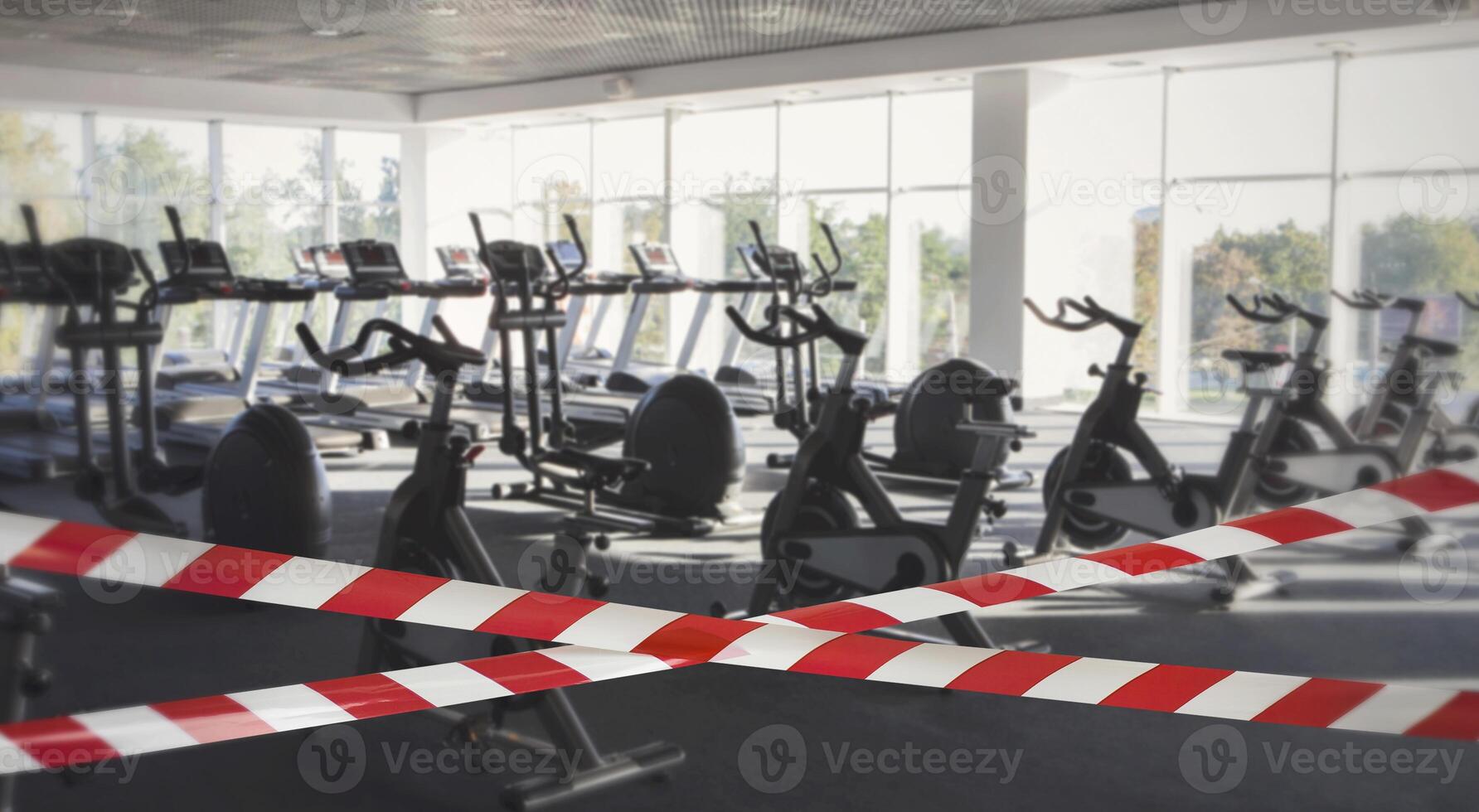 Quarantine Zone Warning Tape, Do Not Cross. Red and white hazard safety stripes across empty closed gym club center photo