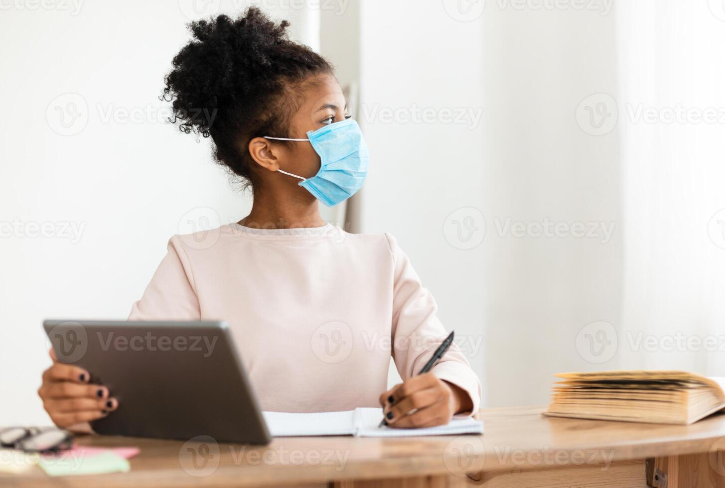 African Girl In Protective Face Mask Studying Using Tablet Computer In Classroom. Safe Back To School. Selective Focus photo