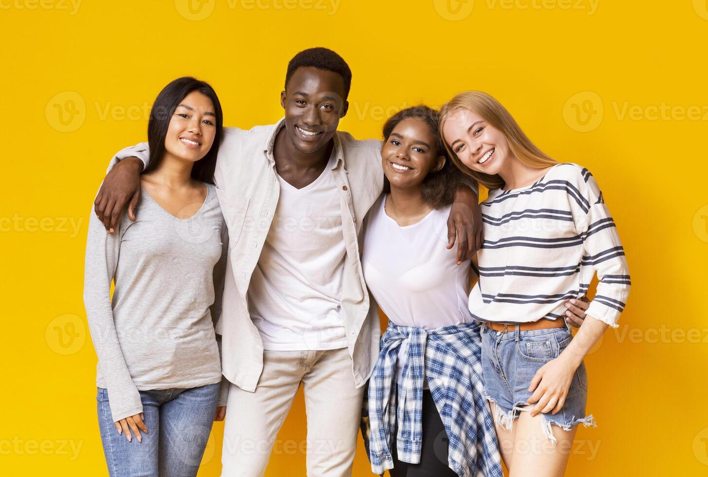 Positive multiethnic group of teenagers posing over yellow studio background photo