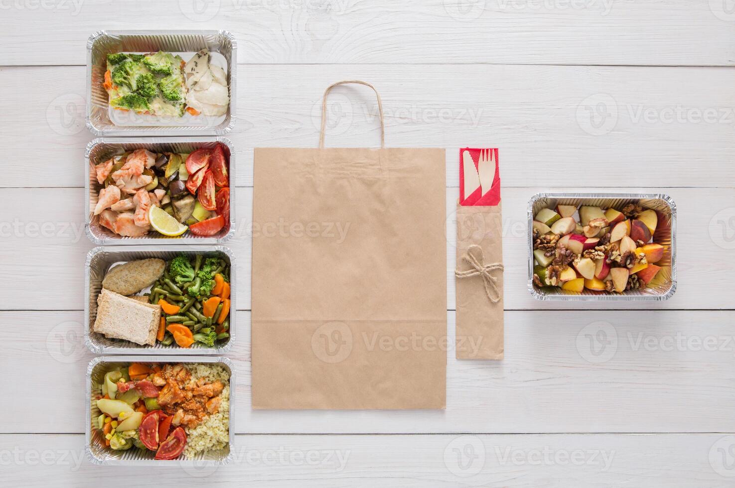 Healthy food delivery. Take away of natural fitness dishes for diet. Daily meals in foil boxes on white wood. Vegetables, salmon, meat and salads. Top view, flat lay, copy space on craft package photo