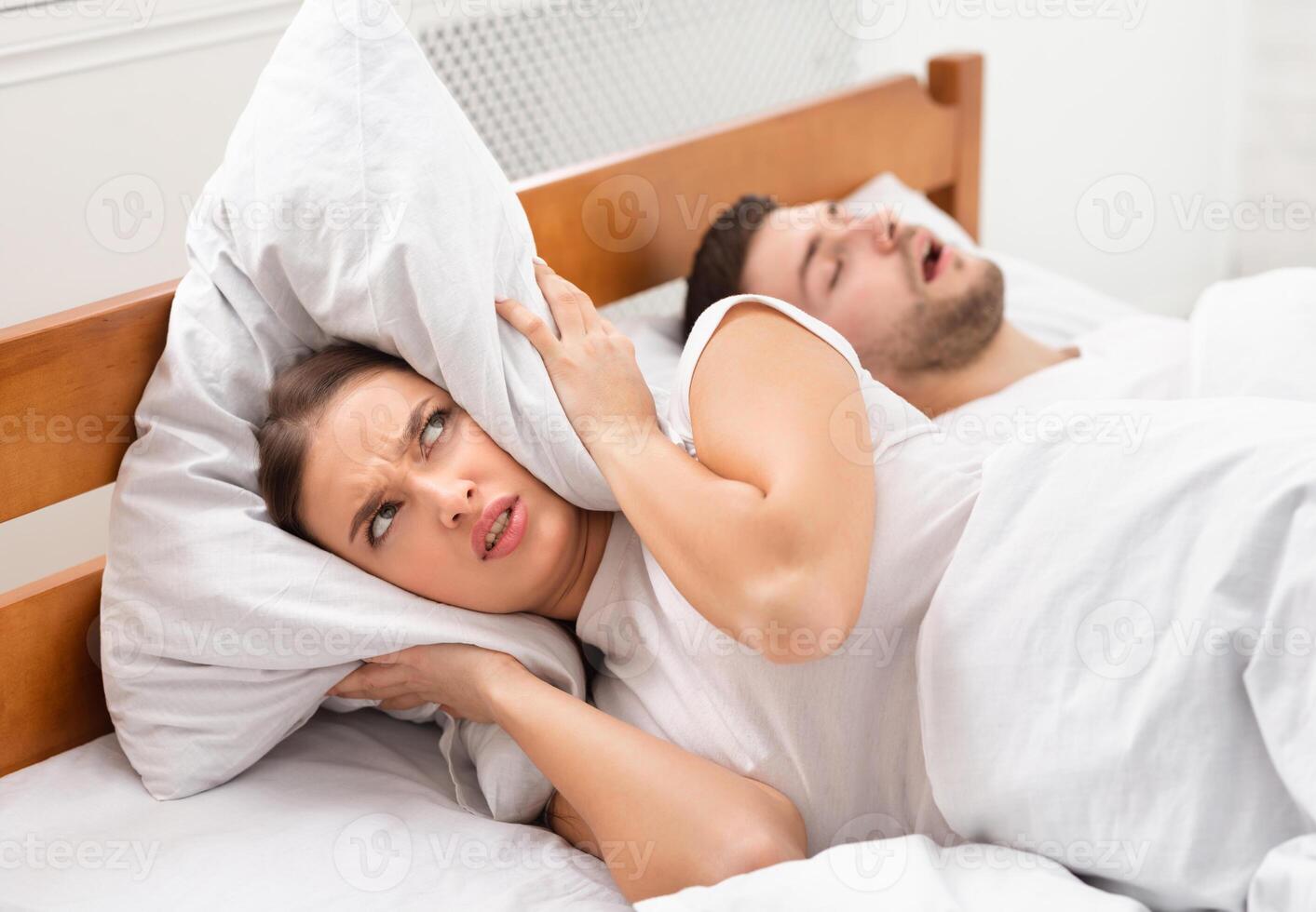 Husband Snoring Bothering Angry Wife Unable To Get To Sleep Covering Ears With Pillow Lying In Bed Indoor. Selective Focus photo