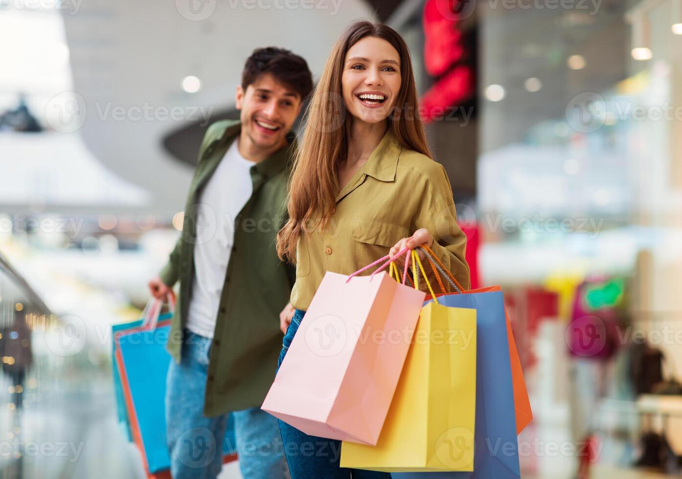 Cheerful Couple Shopping Walking And Carrying Colorful Shopper Bags, Having Fun During Great Seasonal Sales Buying New Clothes Together In Modern Mall. Buyers Spending Weekend In Hypermarket photo