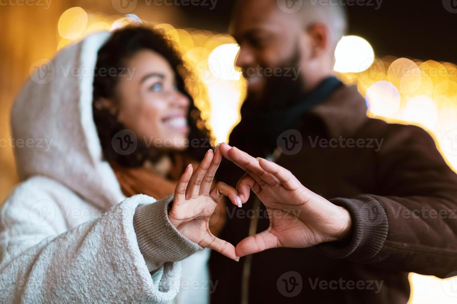 Love, Affection And Bonding Concept. Closeup outdoor portrait of happy smiling black african american couple making heart shape with hands walking together in the evening, looking at each other photo
