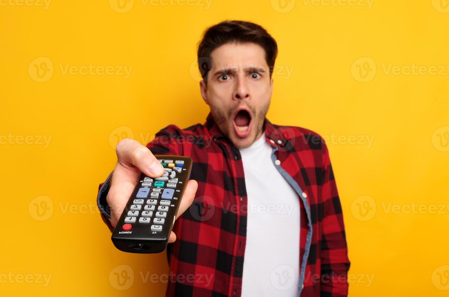 Omg, Unbelievable. Portrait of scared guy watching TV show or film, holding remote control, switching channels, selective focus. Young frightened man feeling fear or surprise during thrilling moment photo