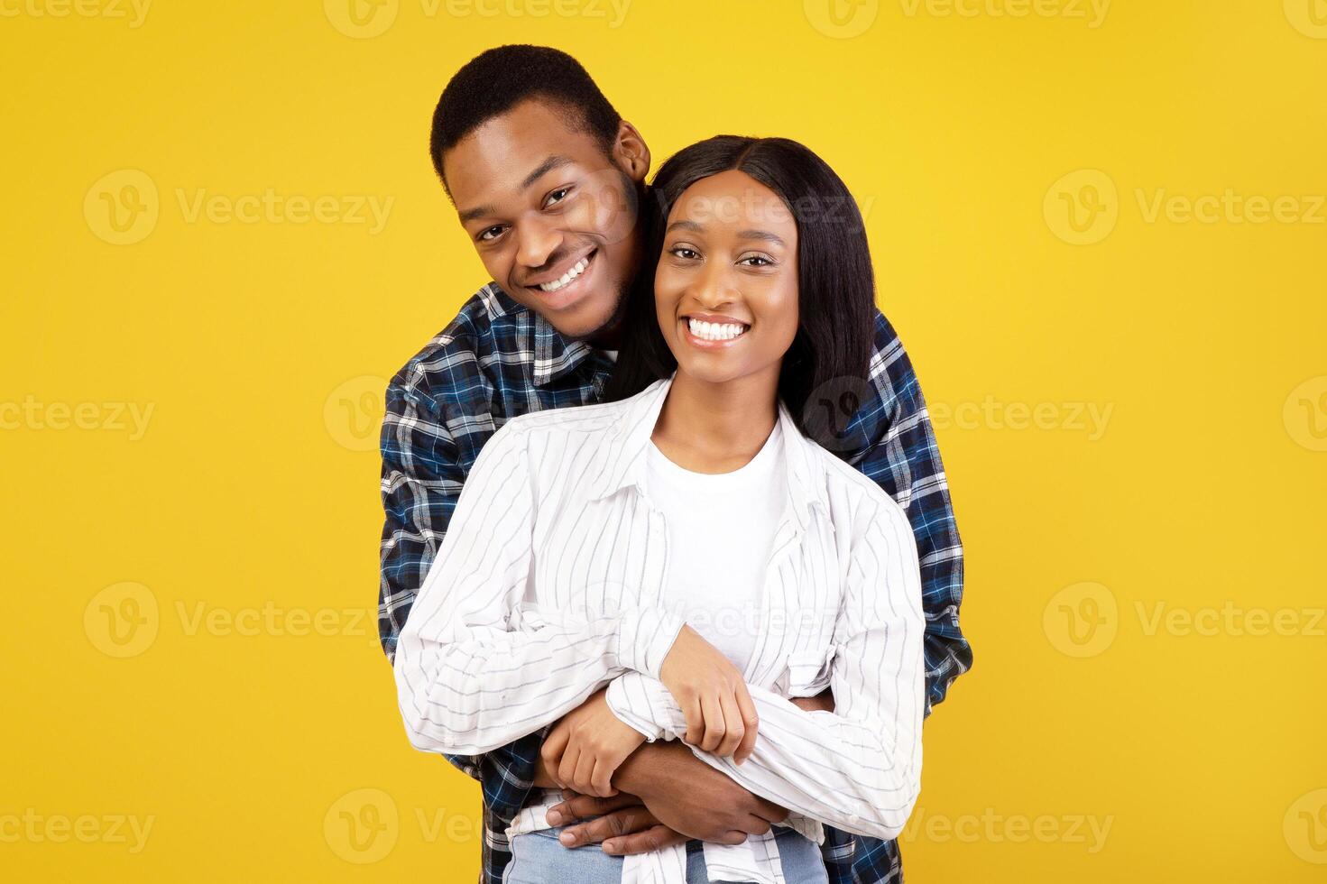 Happy romantic date or self-isolation together. Cheerful young african american male and female in casual, hugging and looking at camera, isolated on yellow background, studio shot, copy space photo