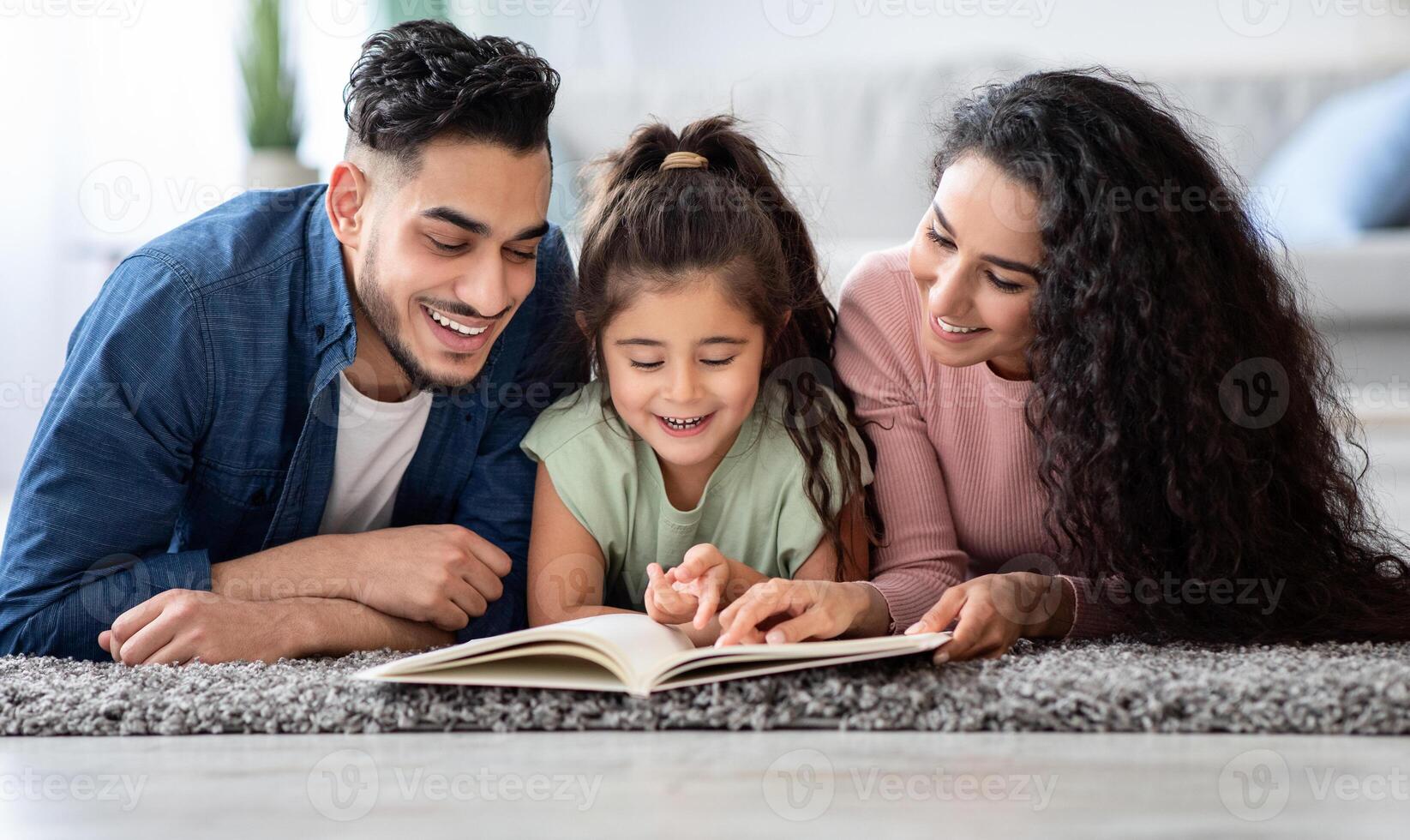 Portraif Of Happy Arabic Family Of Three Reading Book Together At Home, Relaxing On Floor In Living Room, Middle Eastern Mom And Dad Spending Time With Their Kid, Enjoying Domestic Leisure, Closeup photo