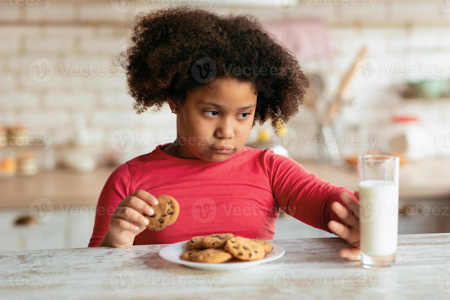 Grumpy Little Black Girl Refusing Milk And Eating Cookies In Kitchen, African Female Kid Choosing Fresh Baked Chocolate Biscuits Instead Of Healthy Calcium Drink While Having A Bite At Home, Closeup photo