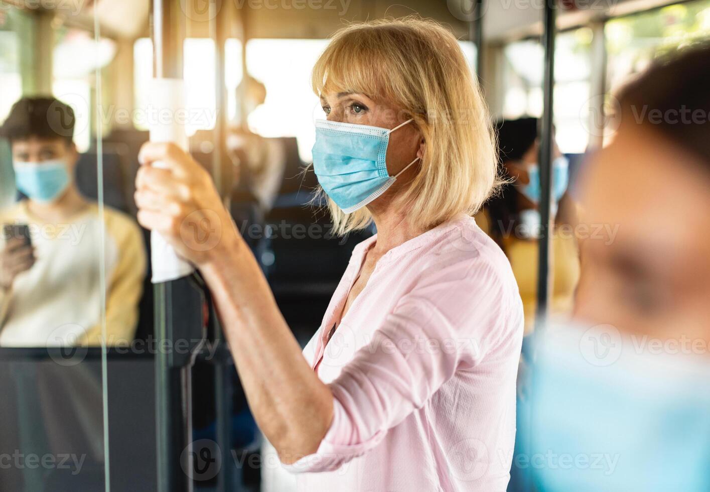 Safe Ride. Portrait of serious senior woman wearing protective face mask taking crowded bus holding handle, standing inside and looking out of window. Rush hour traffic, new normal life rules, covid photo