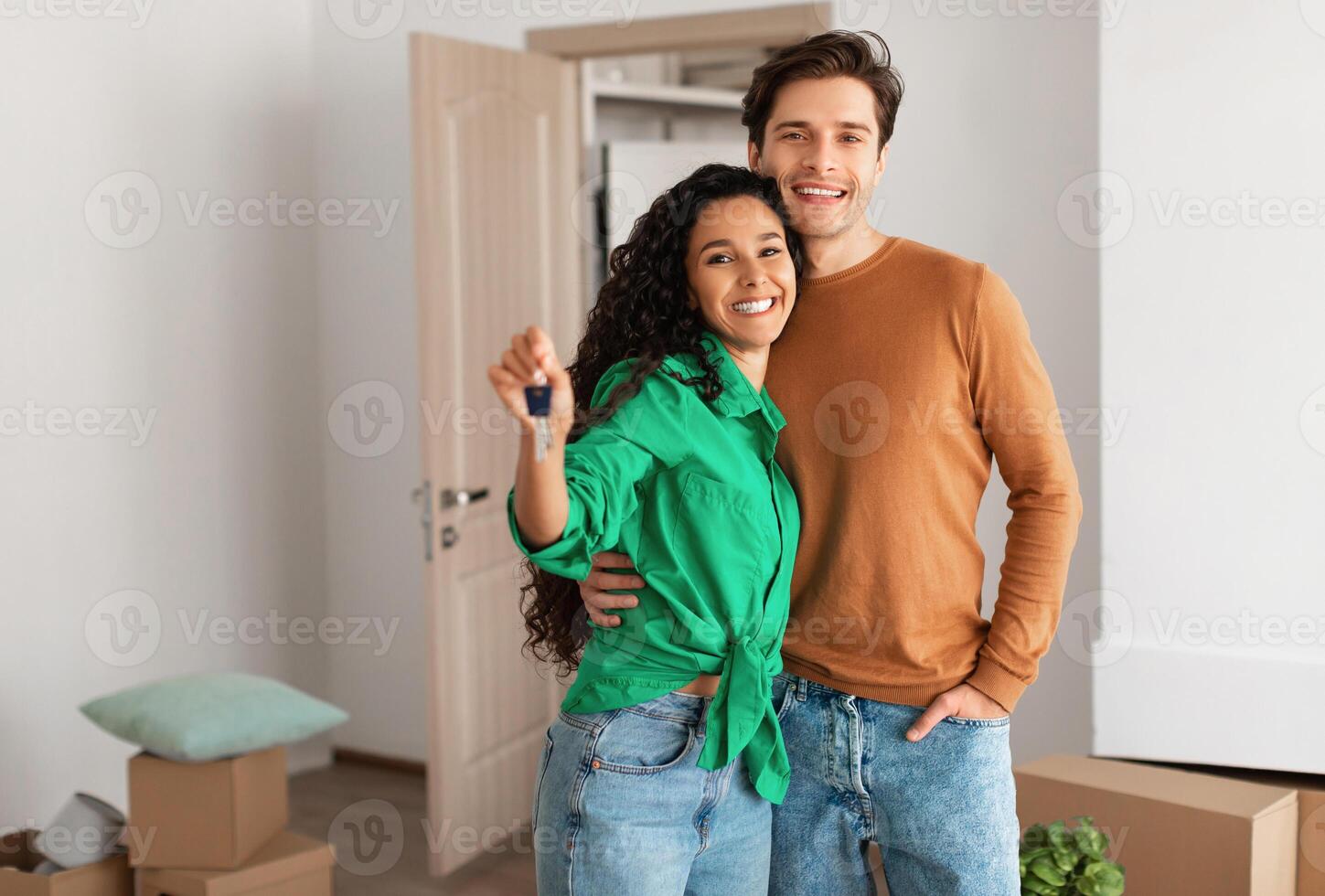 House Ownership. Portrait Of Happy Young Couple Holding Showing Key Standing In New Flat, Cheerful Guy Embracing Lady Posing After Moving In Own Apartment. Insurance, Real Estate, Mortgage Concept photo