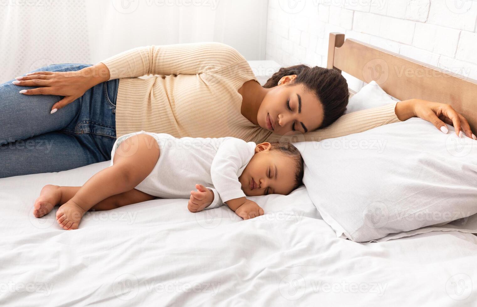 African Mother And Her Baby Son Sleeping During Daytime Sleep Lying In Bed In Modern Bedroom At Home. Tired Mommy Resting Near Her Little Toddler Napping Indoor. Side View photo