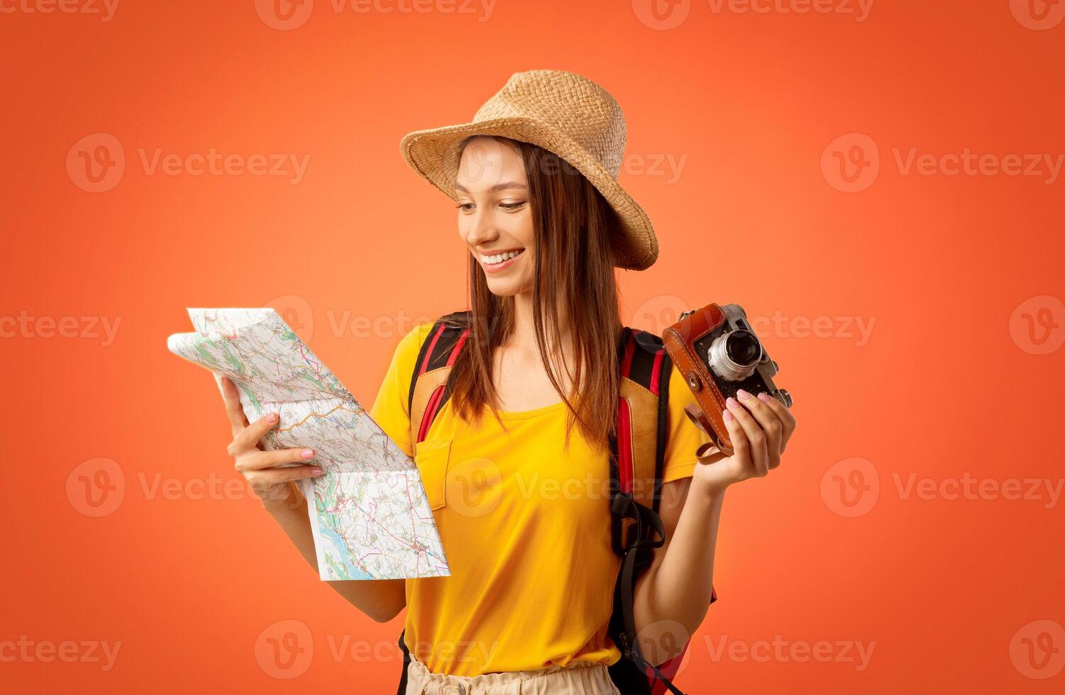 Happy girl traveller with camera looking at map, yellow studio background photo