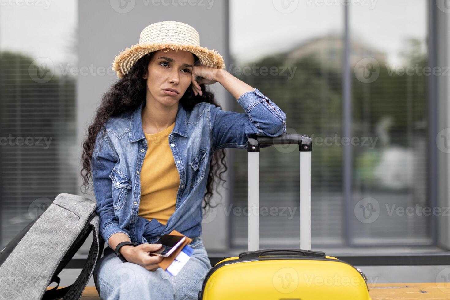 Canceled or delayed flight, difficulties while travelling. Upset young woman tourist waiting for flight at airport, holding documents, phone, touching her head, feeling stressed, looking at copy space photo