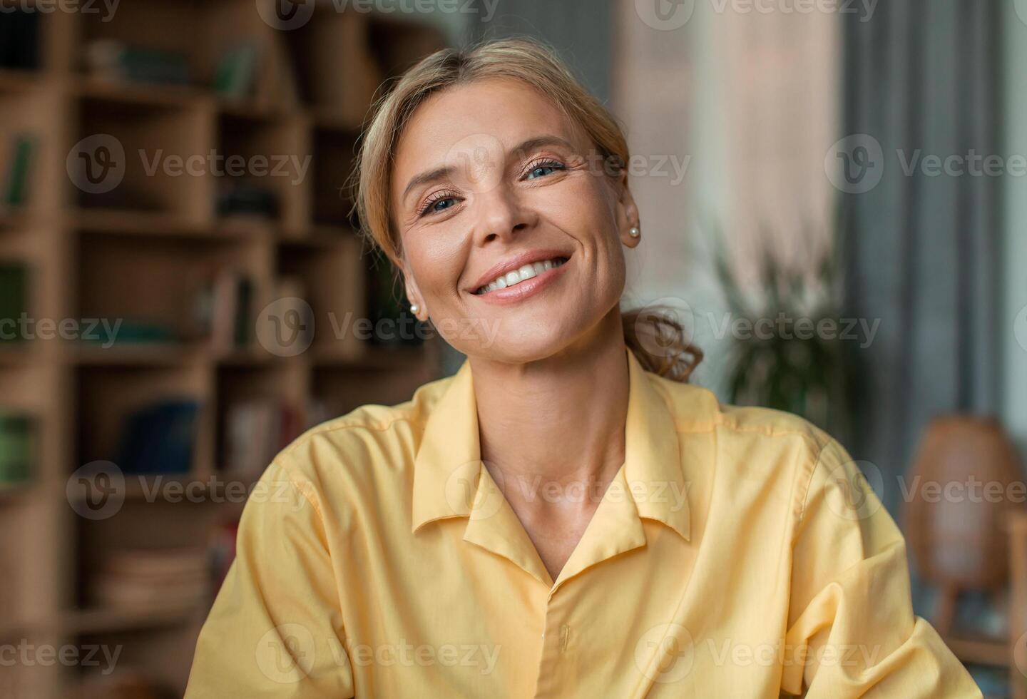 Portrait of positive middle aged female psychologist talking to camera and smiling during therapy session in office. Friendly psychotherapist posing in cabinet photo