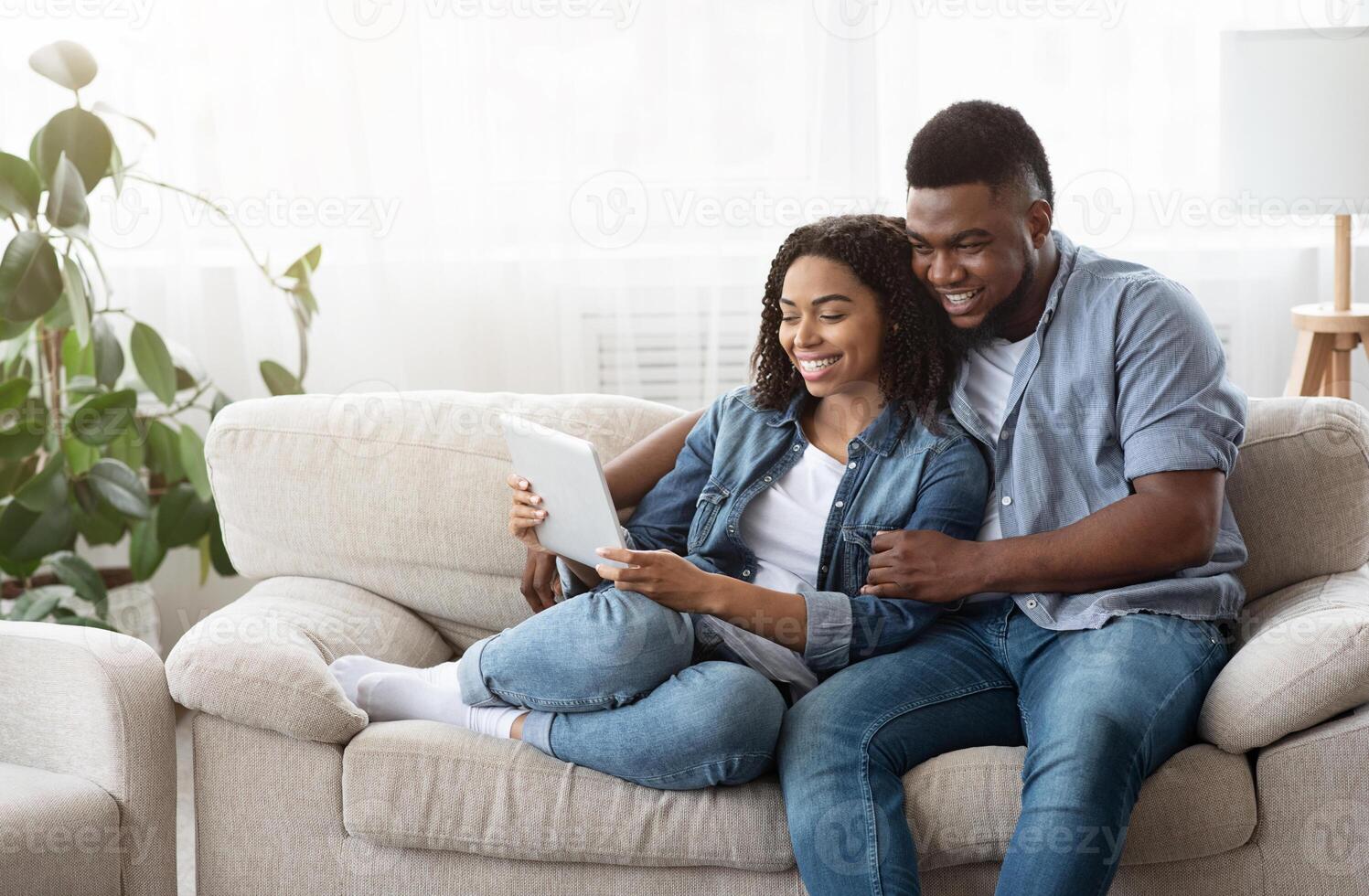 Quarantine Leisure Concept. Happy Black Couple Relaxing With Digital Tablet At Home, Watching Videos Together Or Browsing Internet, Free Space photo