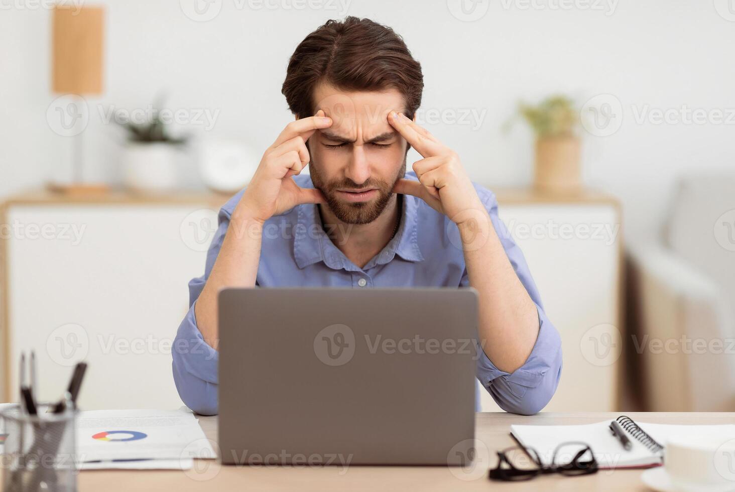 Unhappy Businessman Suffering From Headache Pain Touching And Massaging Aching Head Sitting At Laptop Computer In Modern Office. Health Problem, Painful Migraine Concept. Selective Focus photo